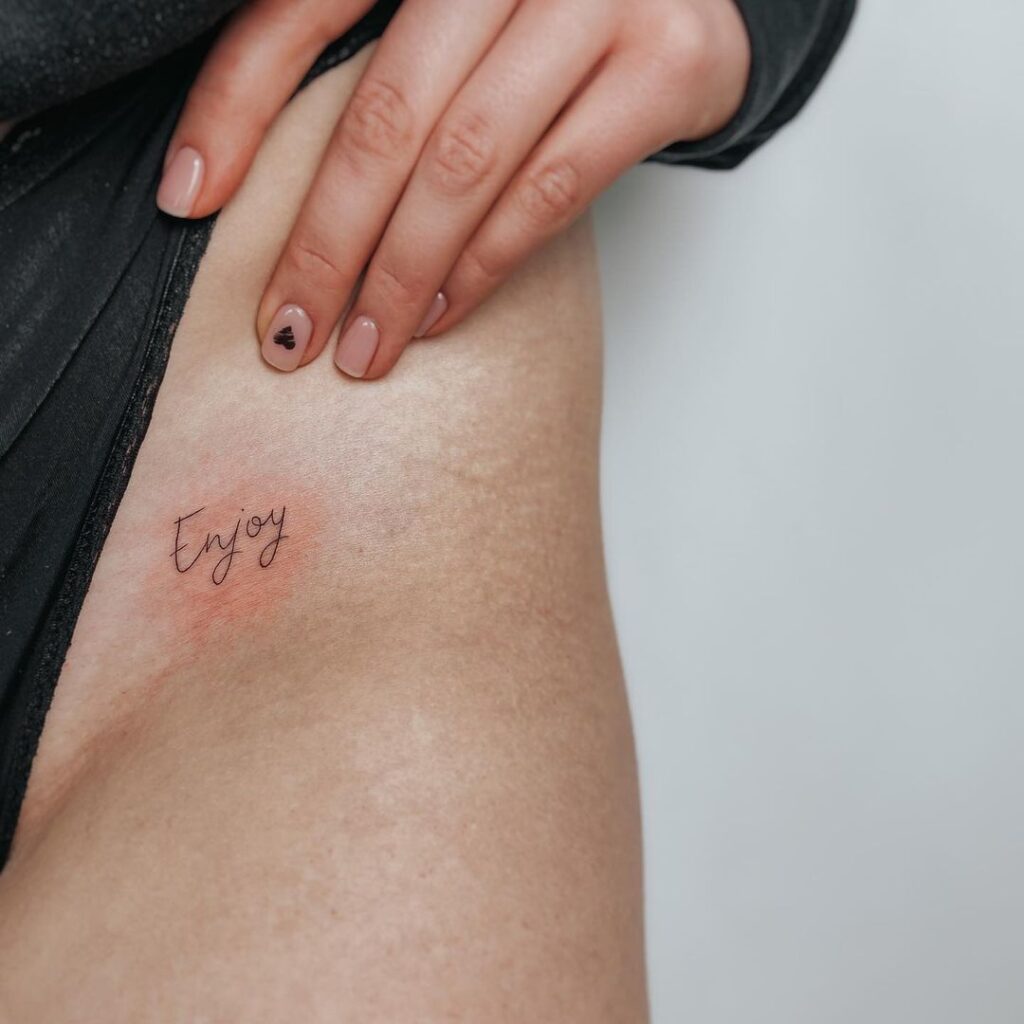 Een tattoo van "enjoy" op de heup